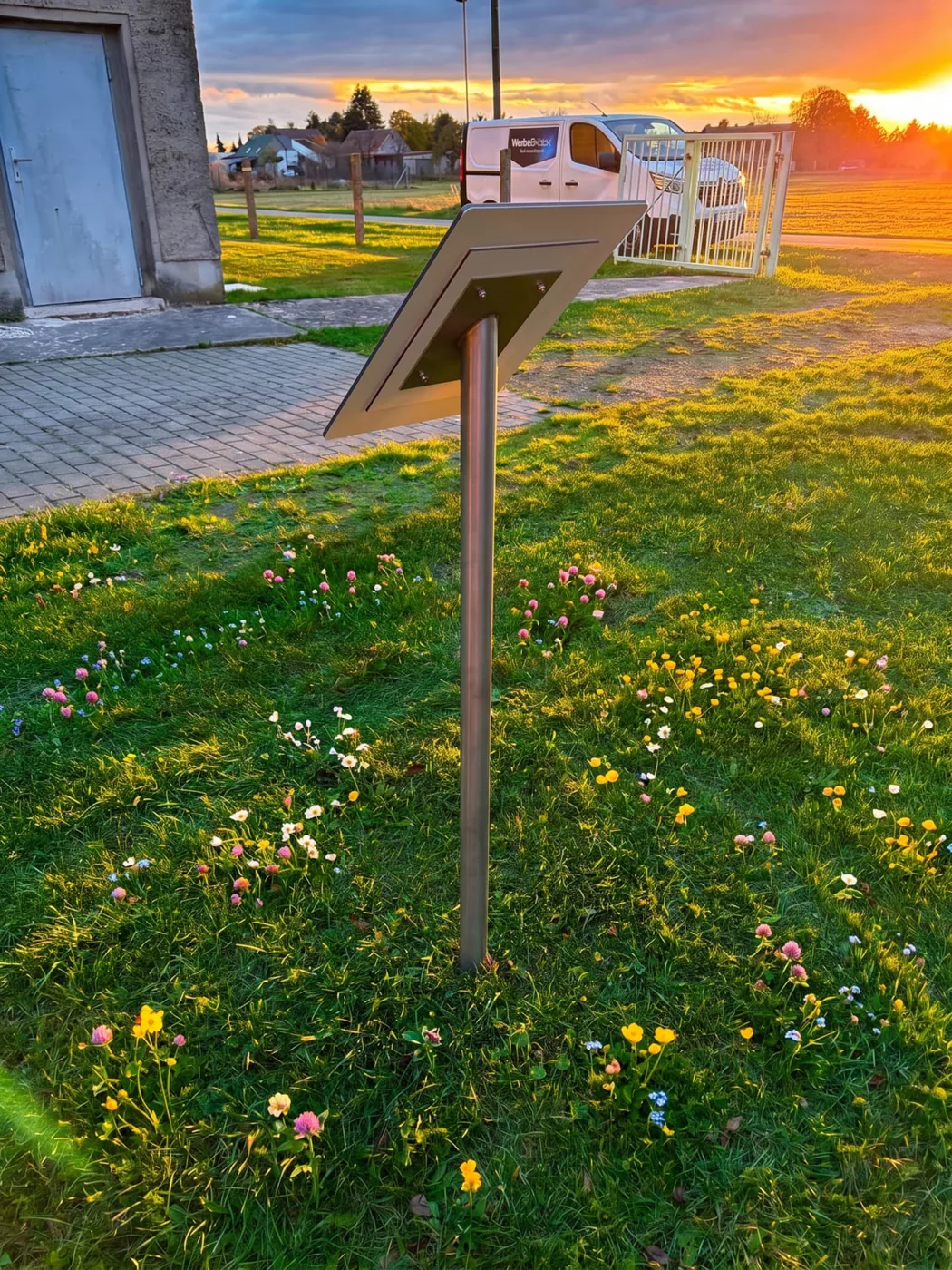 Edelstahl-Pultaufsteller mit fester Platte auf einer Blumenwiese bei Sonnenuntergang