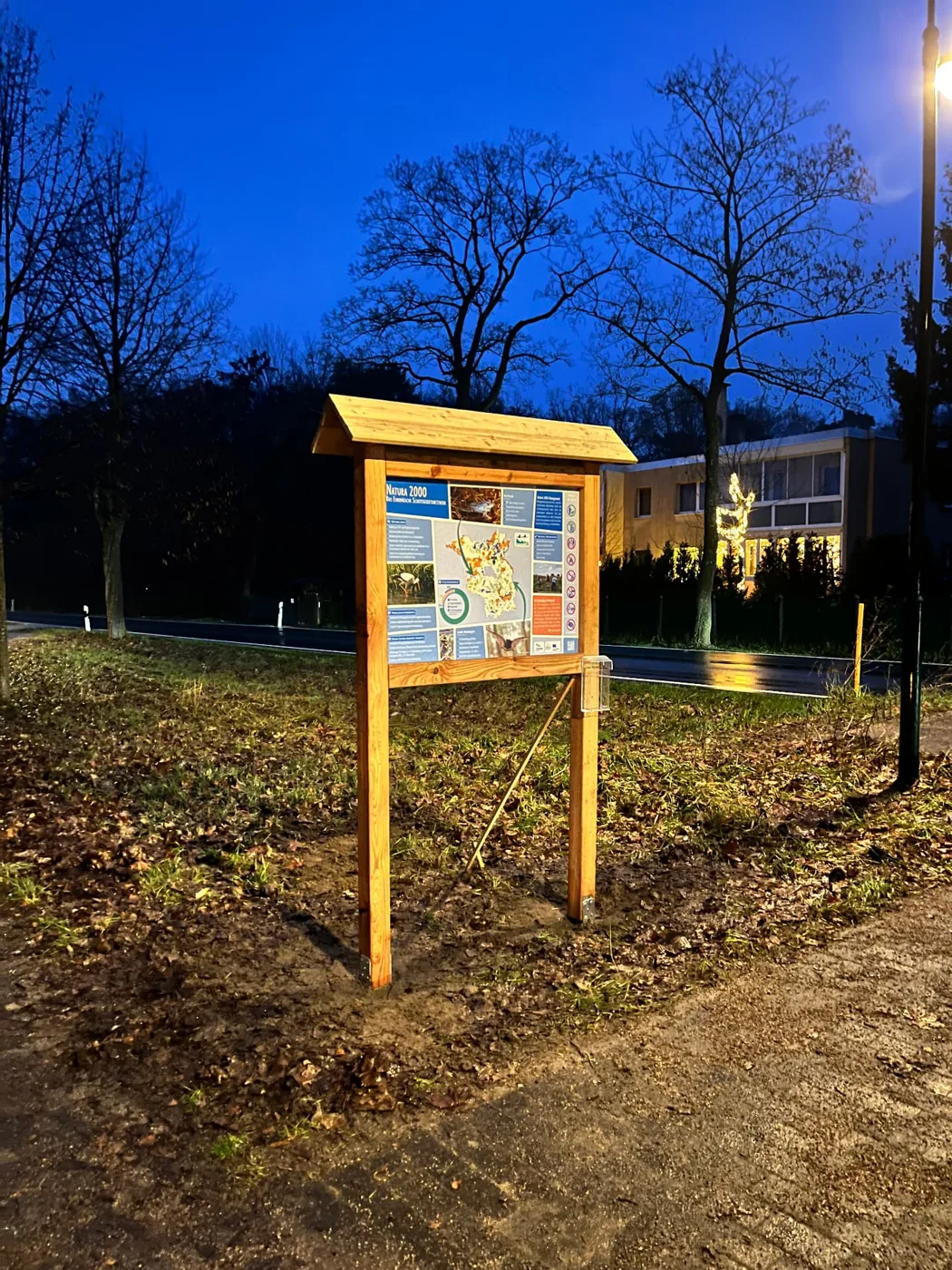 Beleuchtete Holz-Infotafel an einem Lehrpfad am Abend